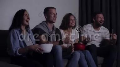四个朋友坐在沙发上，在电视上看有趣的电影。高加索年轻人坐在沙发上，喝着饮料，吃着零食。电影